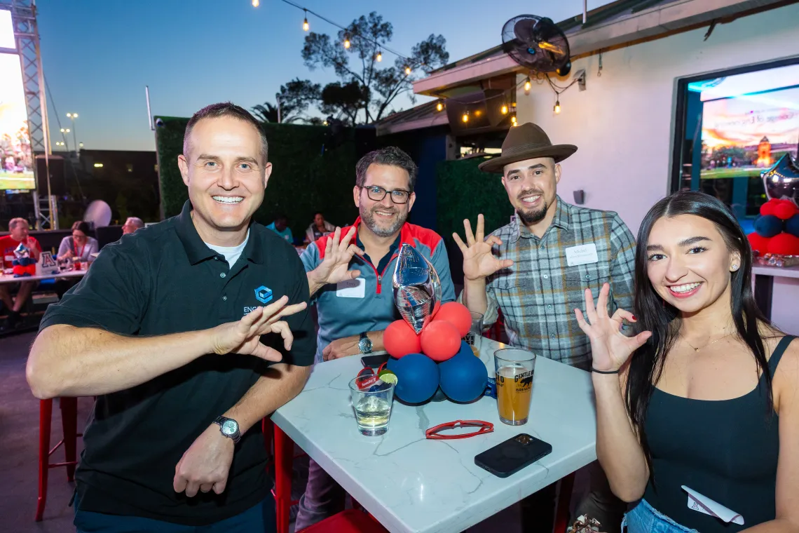 Four individuals smiling and holding up the wildcat symbol 