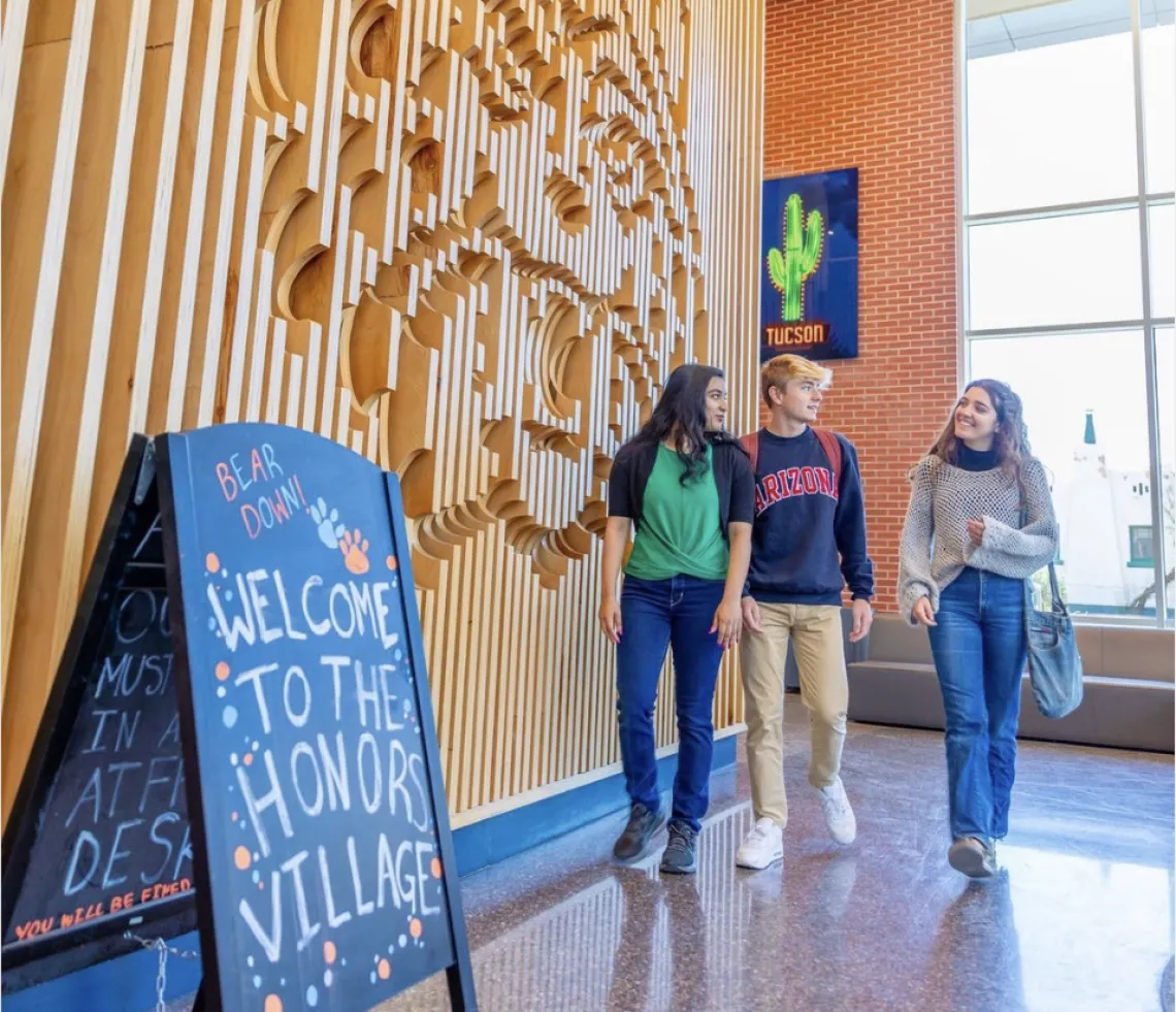 Three students walking in The Honors Village with a sign that reads "Welcome to the Honors Village"