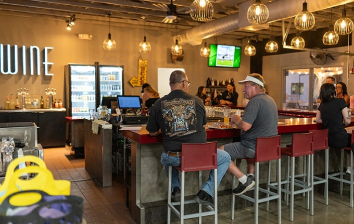 People sitting at a brightly lit bar with a sign in the lefthand corner that says "Wine"