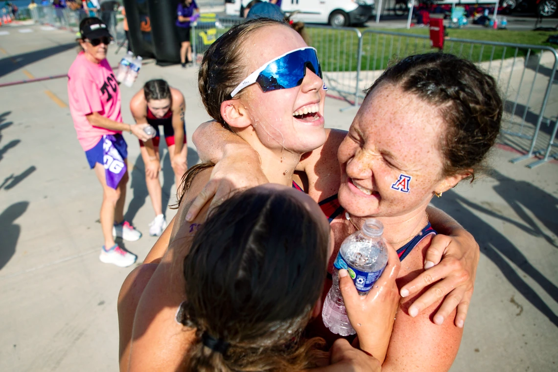 Two Arizona triathletes embrace joyfully at the finish line, drenched and smiling after a race.