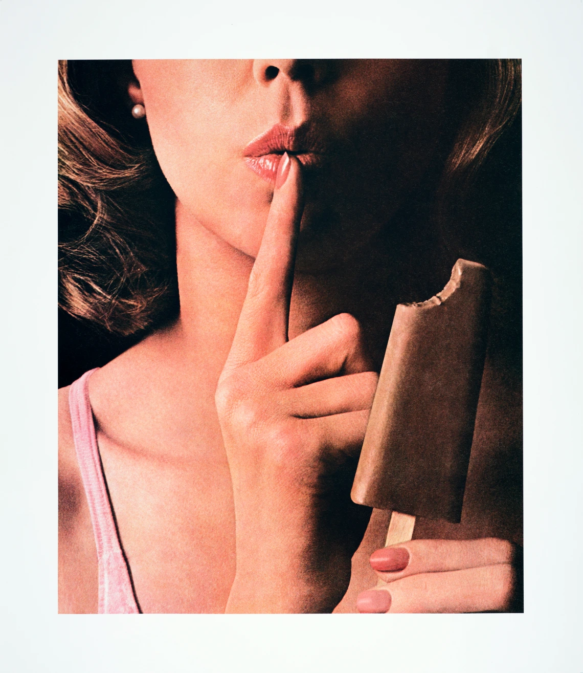 A close-up of a woman’s lips with her index finger pressed to them, holding a bitten chocolate popsicle in her other hand.