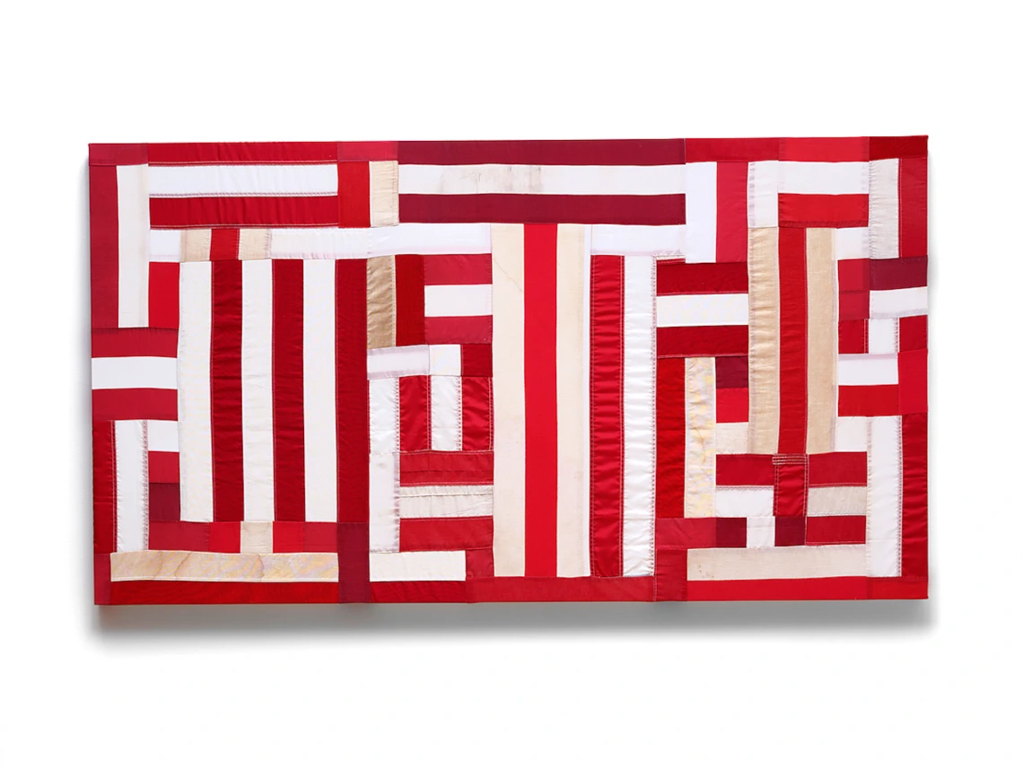 A geometric patchwork artwork composed of red, white, and beige fabric strips, resembling a reimagined flag or quilt.