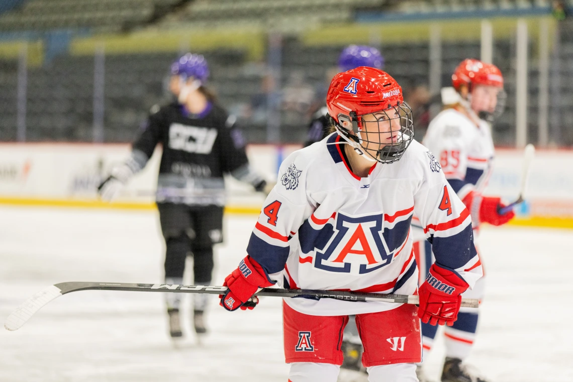 Arizona player in a white and red jersey with number 4 skates across the ice, focused during gameplay.