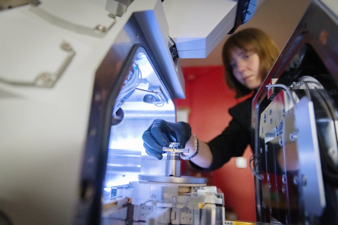 A researcher examines asteroid sample particles in a laboratory, with precision instruments and sterile handling tools visible.