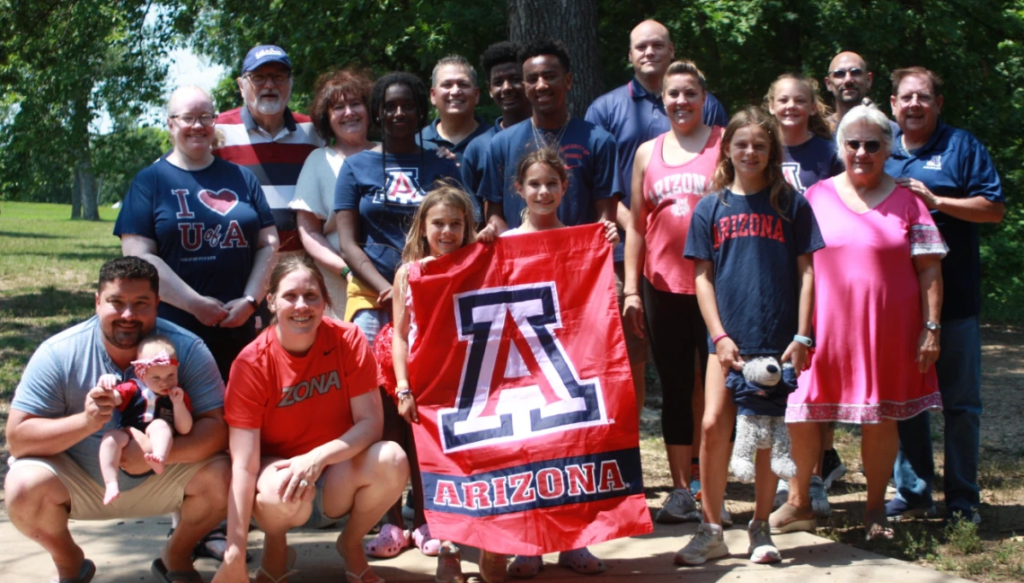 A group of people from all ages smiling and wearing U of A clothing