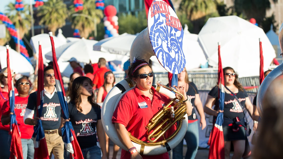 A group of band alumni playing instruments and walking in the Homecoming march