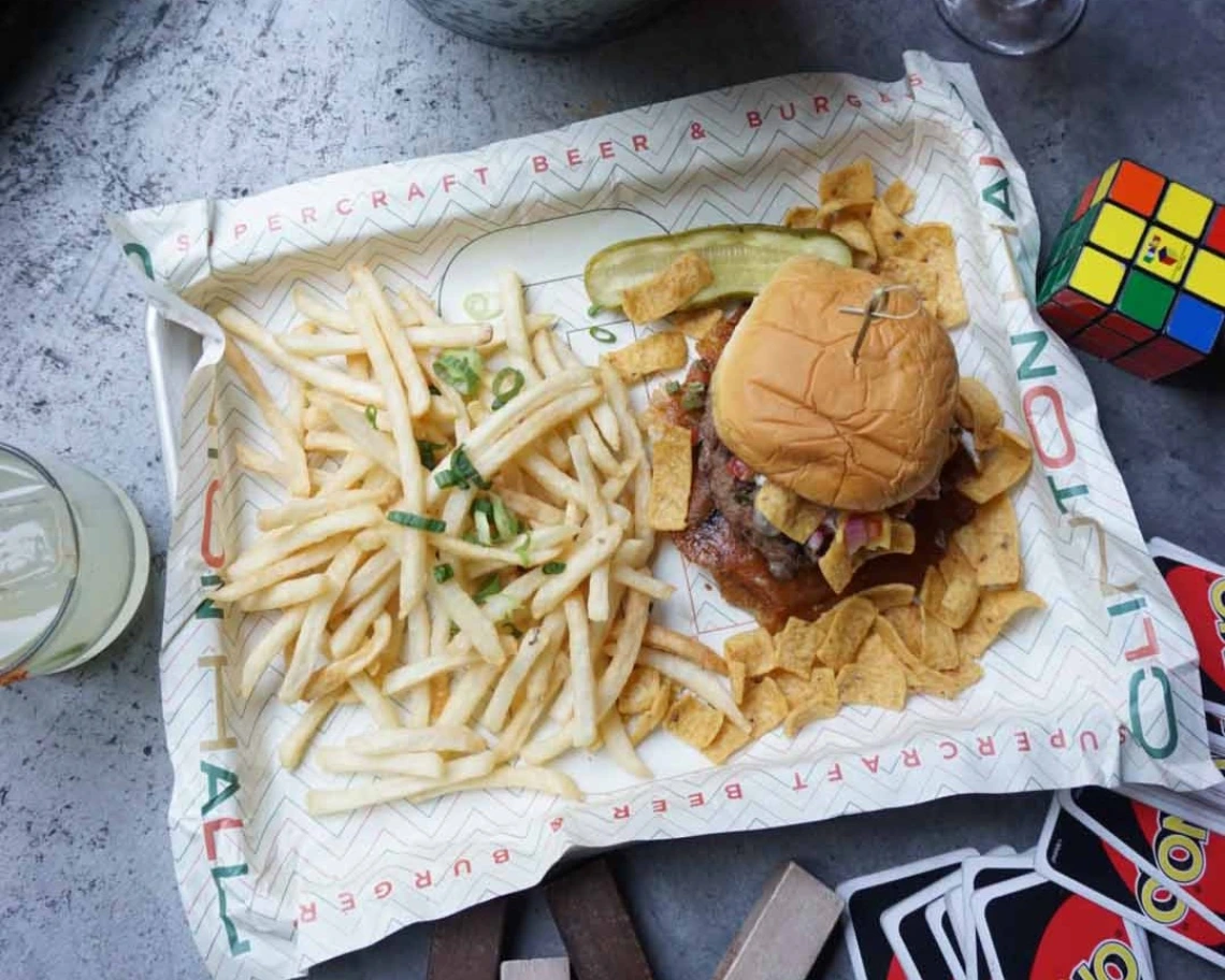 A hamburger and fries, next to a beer and board games