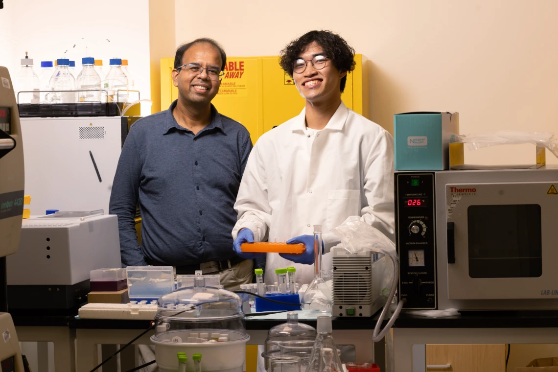 Abhijit Date and Tom Pham smiling and working in the lab. 