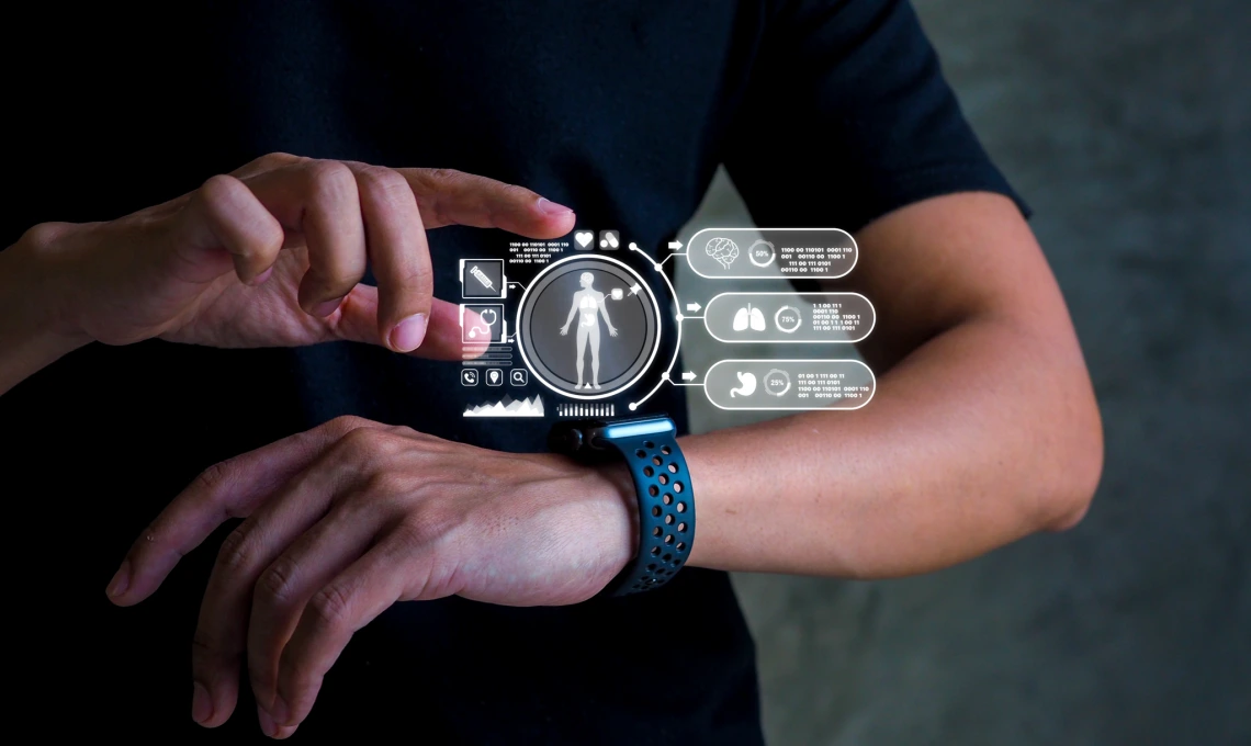 An image of a person wearing a wearable device. The device screen shows a human body with different pieces of information and charts available for viewing. The person's finger is hovering over the heart icon.