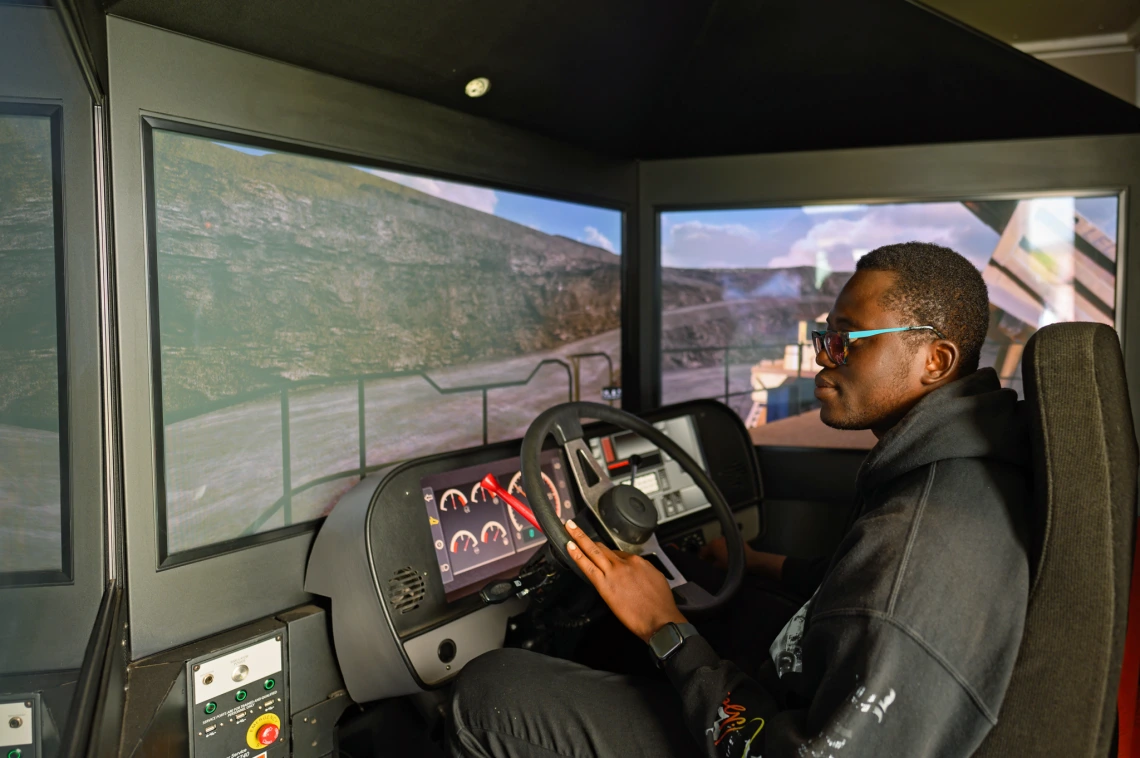 An image of inside a mining truck. The driver is seen making a left and the mine is in the background.