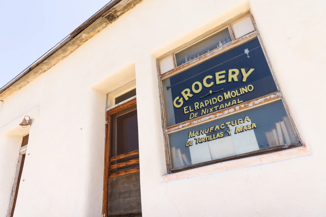 A white building with the words, "Grocery El Rapido Molino De Nixtamal, Manufactura de Tortillas Y Masa" written on the window.