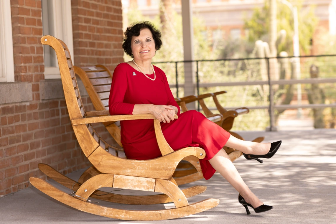 Patricia Prelock sitting on a rocking chair located on the balcony of Old Main.