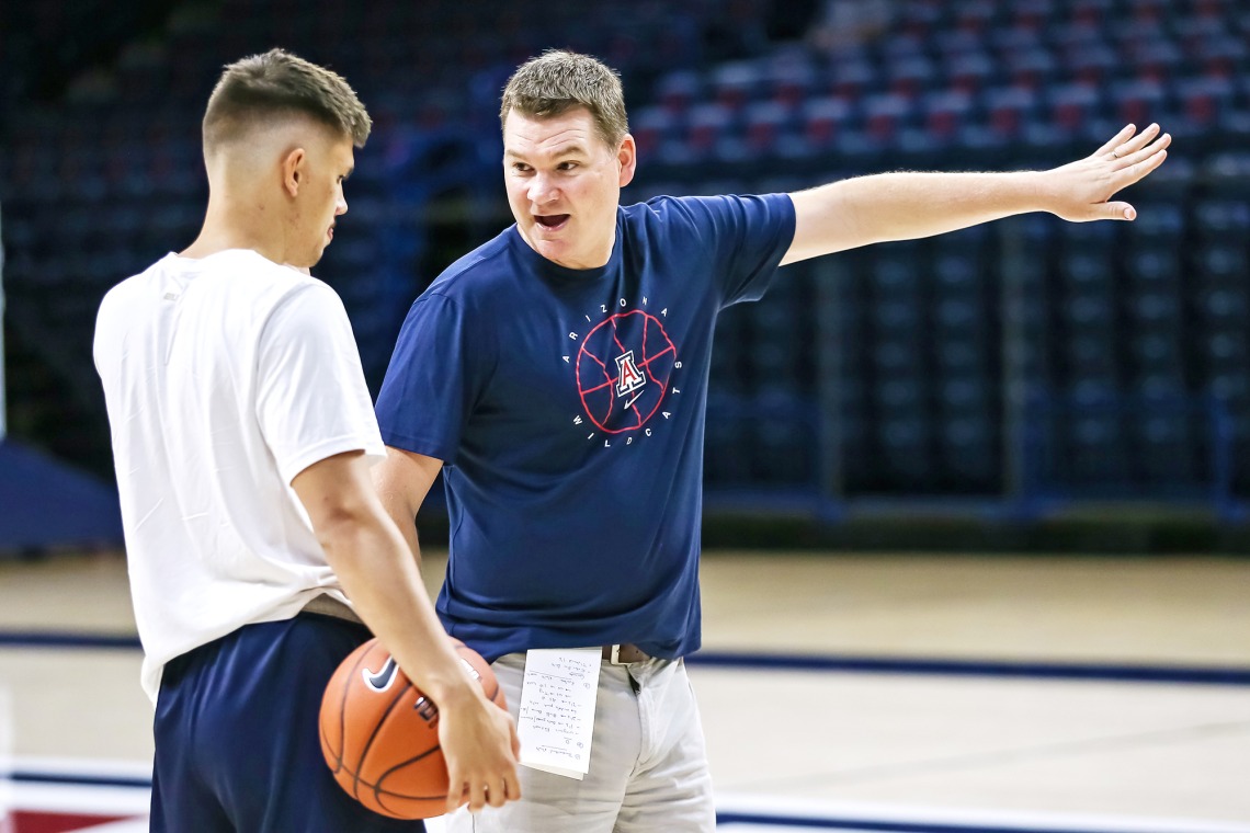 A photograph of Tommy Lloyd, the current University of Arizona basketball coach, speaking with a basketball player.