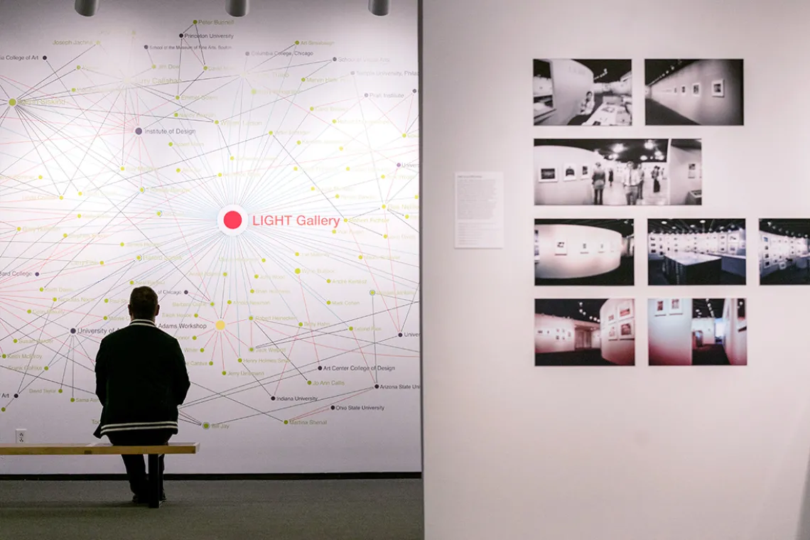 A photograph of a man sitting on a bench and looking at an art instillation 