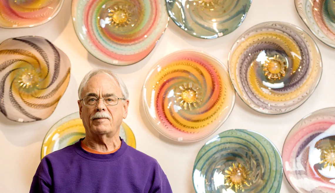 A photograph of Tom Philabaum standing in front of glass plates