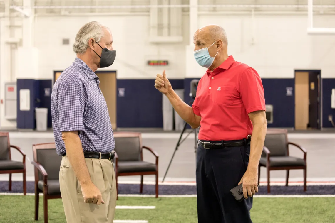 A photograph of Robert C. Robbins and Richard Carmona speaking with masks on in a social distanced space