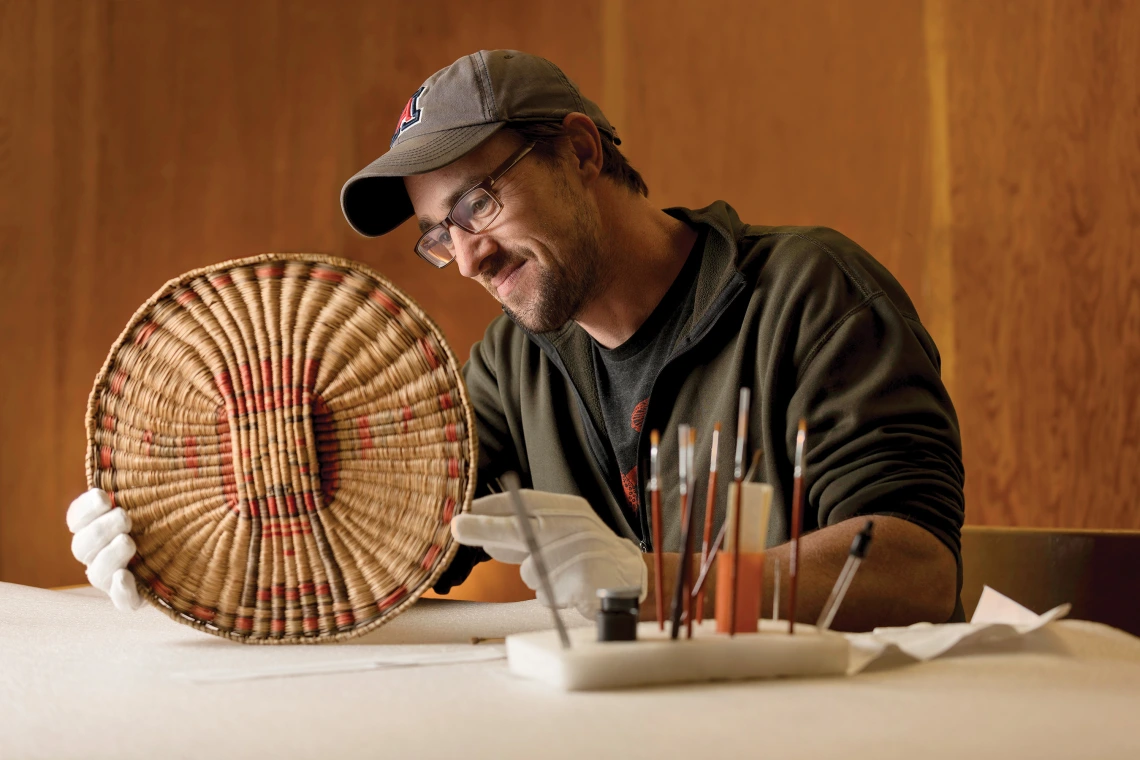 A photograph of Patrick D. Lyons smiling while examining a Hopi artifact