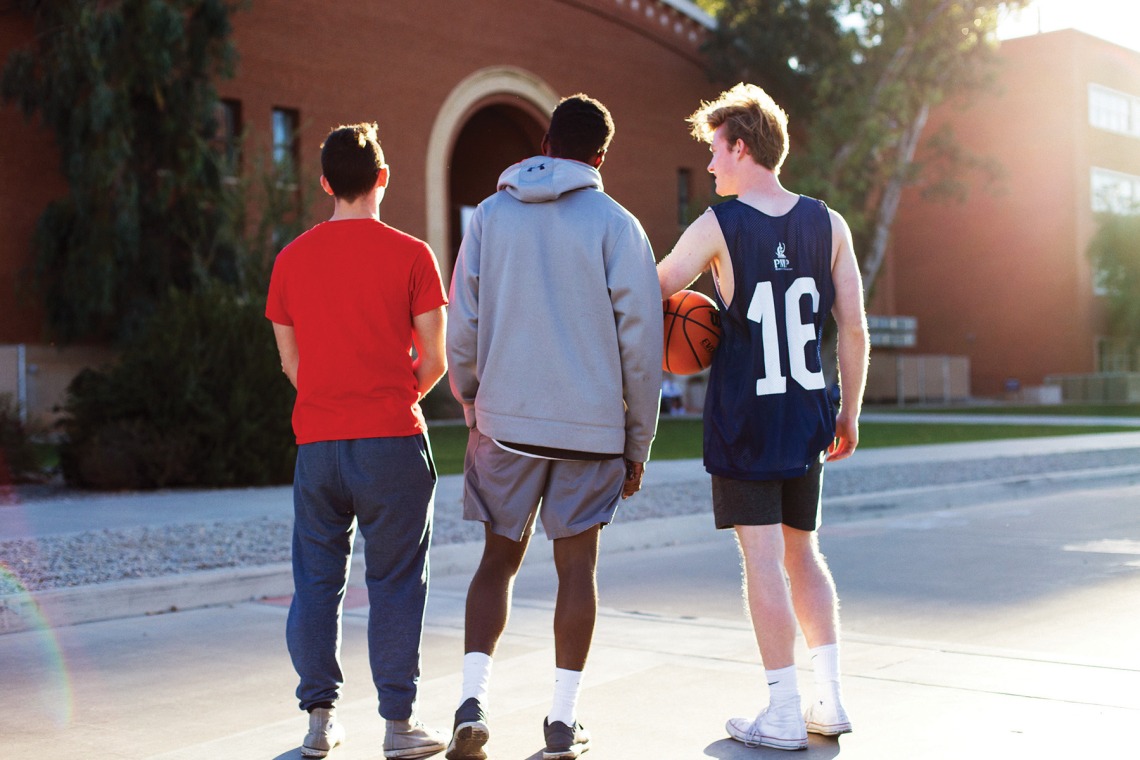 A photograph of three students walking towards Bear Down Gym holding a basketball