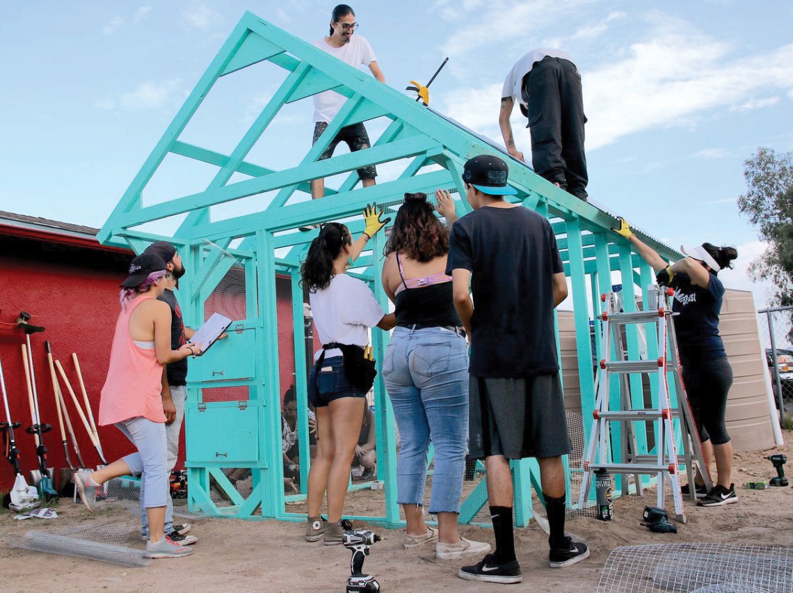 A photograph of students coming together to build a teal chicken coop