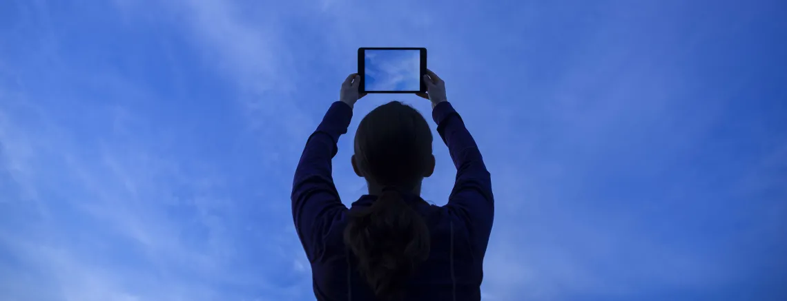 A photograph of a man pointing a blue phone to the blue sky