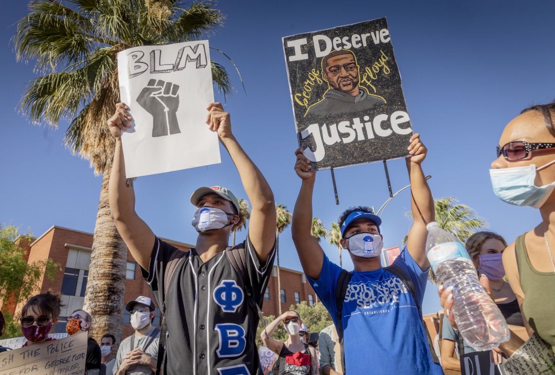 A photograph of attendees holding up a "Black Lives Matter" sign and "I Deserve Justice" George Floyd poster