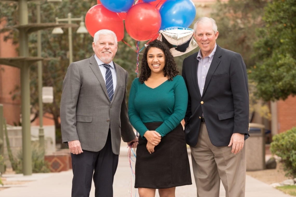 A photograph of Leah Crowder in the middle of Dean Terry Hunt and Dr. Robert C. Robbins, with balloons in the background.