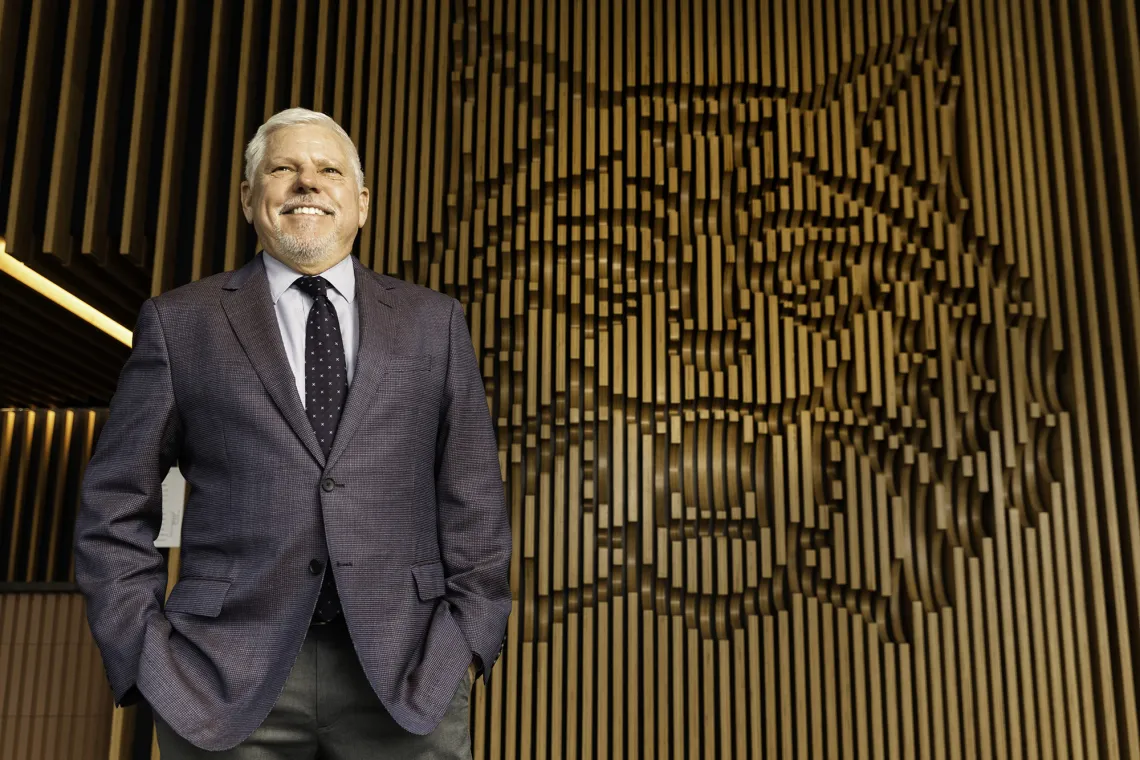 A photograph of Terry Hunt, looking up, smiling and standing in front of a carved out wildcat head symbol