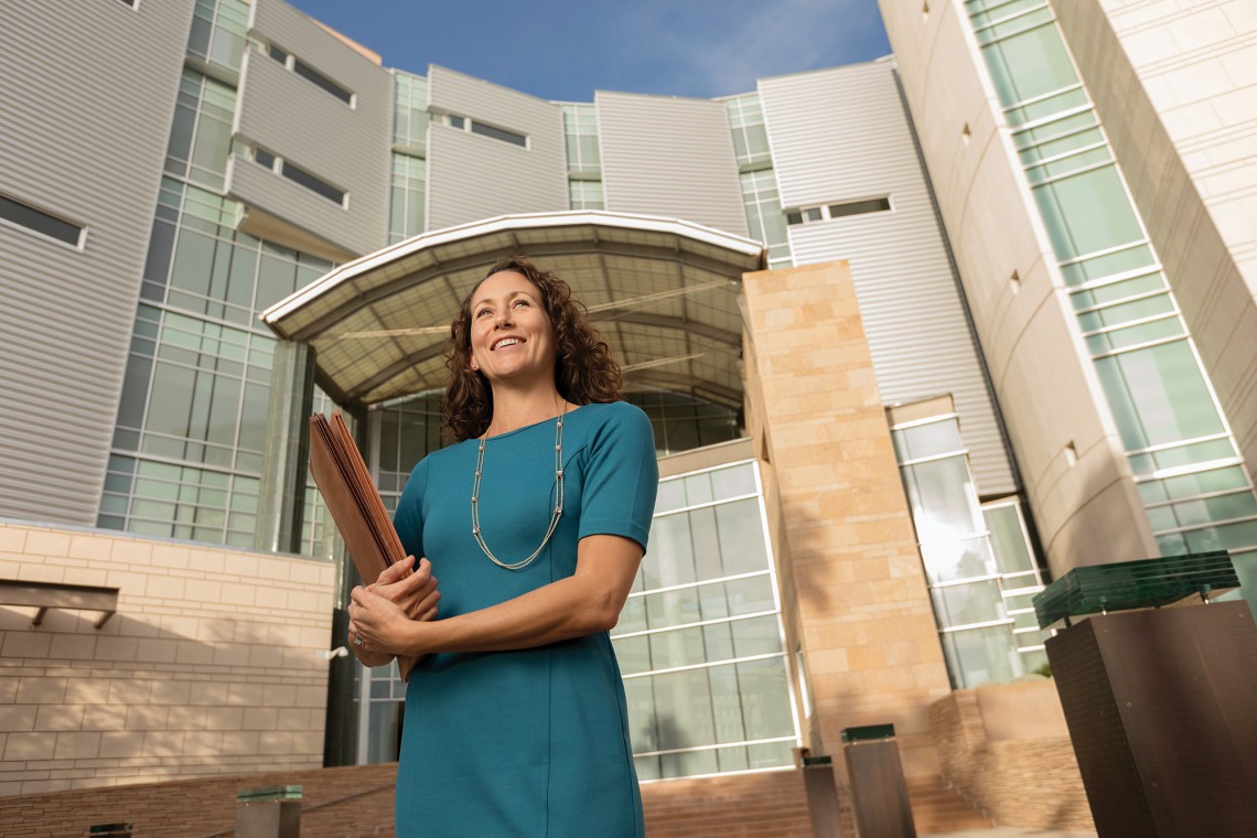 A photograph of Stacy Rupprecht Butler standing in front of a building holding a folder