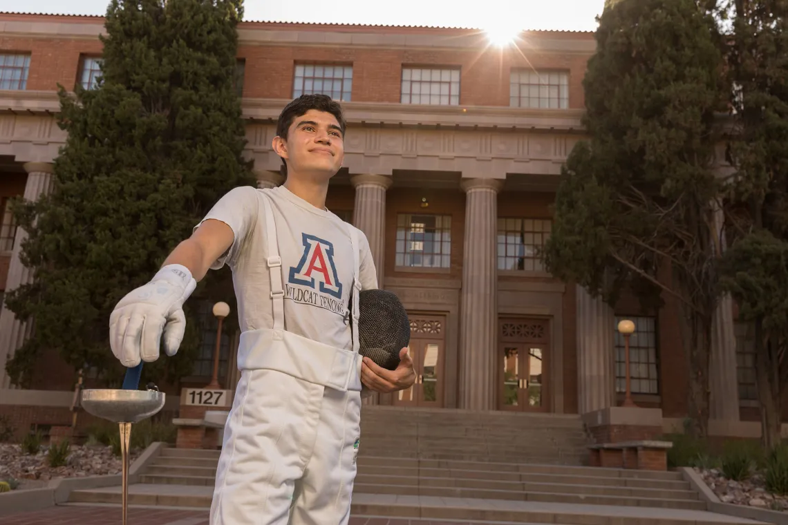 A photograph of Justin Palacios standing, smiling and holding a fencing blade