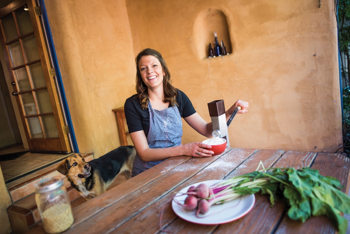 A photograph of Megan Kimble sitting outside making flour, her dog and a set of radishes are near her 