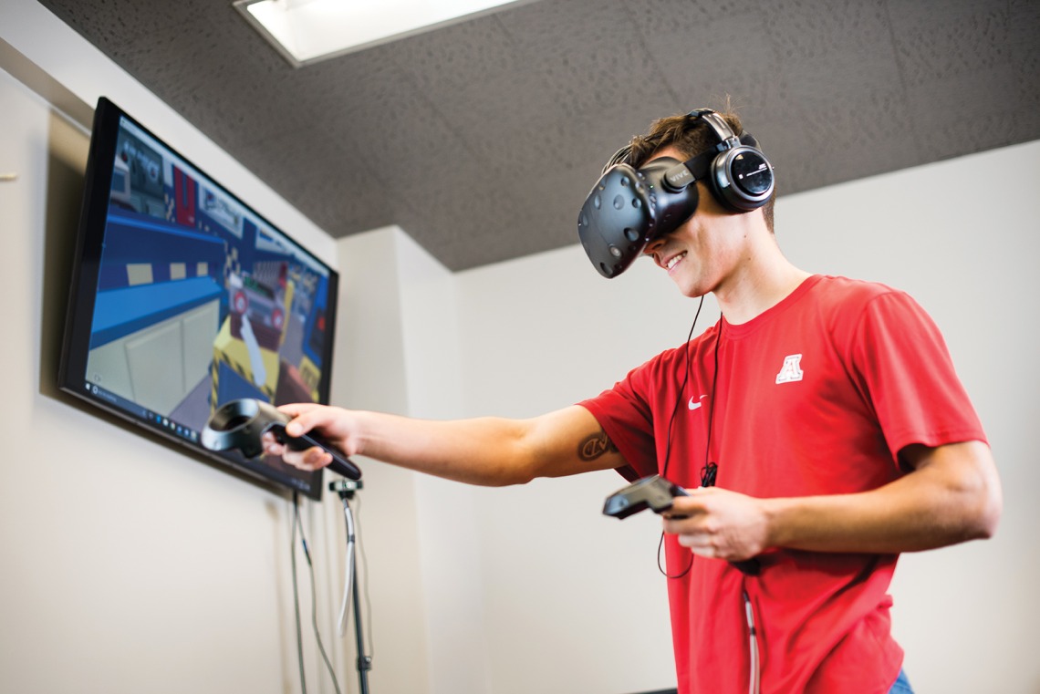 A photograph of a student using a headset and controllers to run a game on-screen
