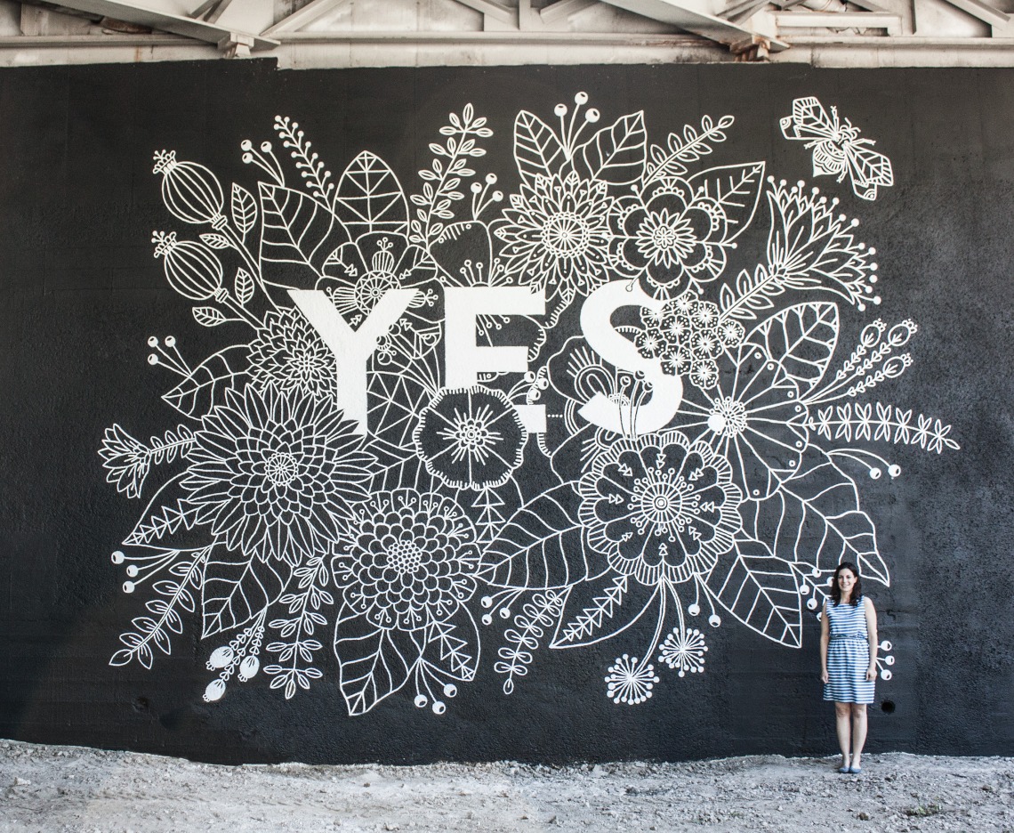 A photograph of Margaret Kimball standing next to her 'YES' mural