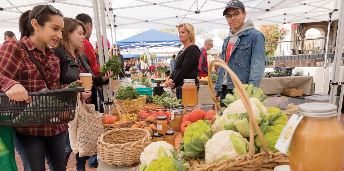A photograph of buyers and sellers looking at fresh produce and chatting at the farmer's market