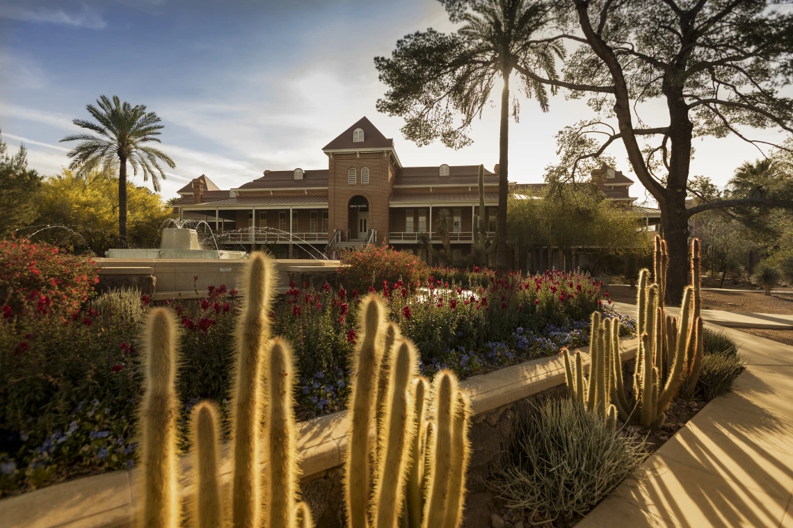 A photograph of Old Main, with the sun peeking out behind it