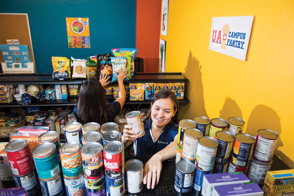A photograph of volunteers stacking canned goods and snacks at Campus Pantry
