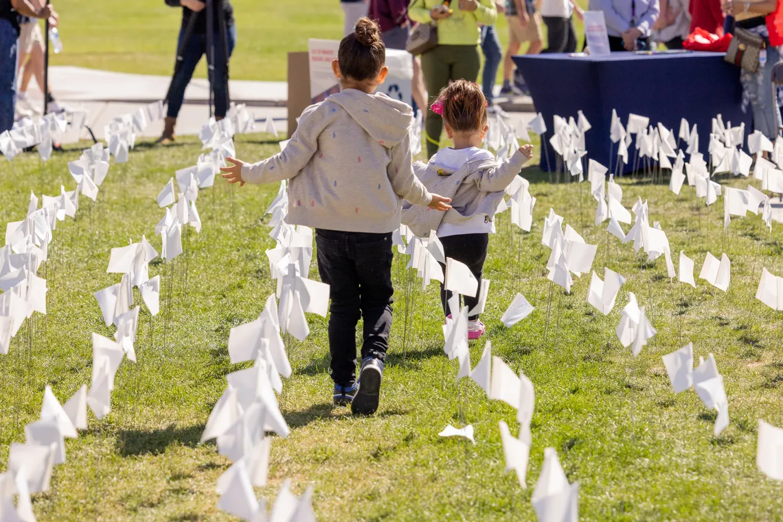 A photograph of two young girls running through a green field with white flags.