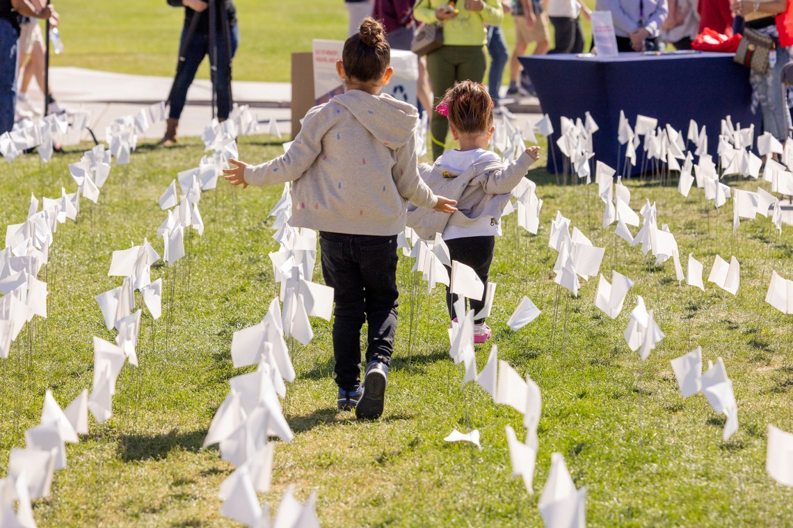 A photograph of two young girls running through a green field with white flags.