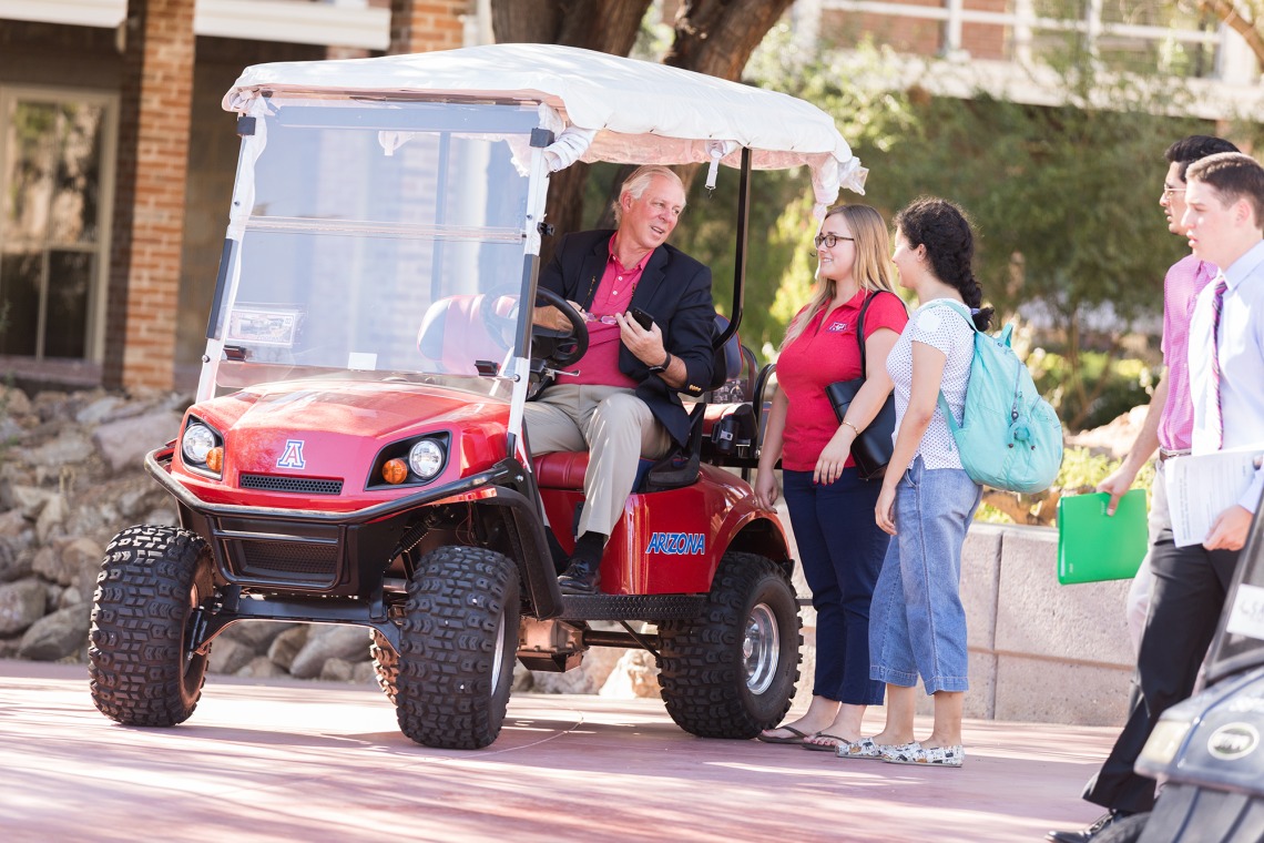 A photograph of President Robbins in a golf cart, stopping to chat with students and staff in front of Old Main
