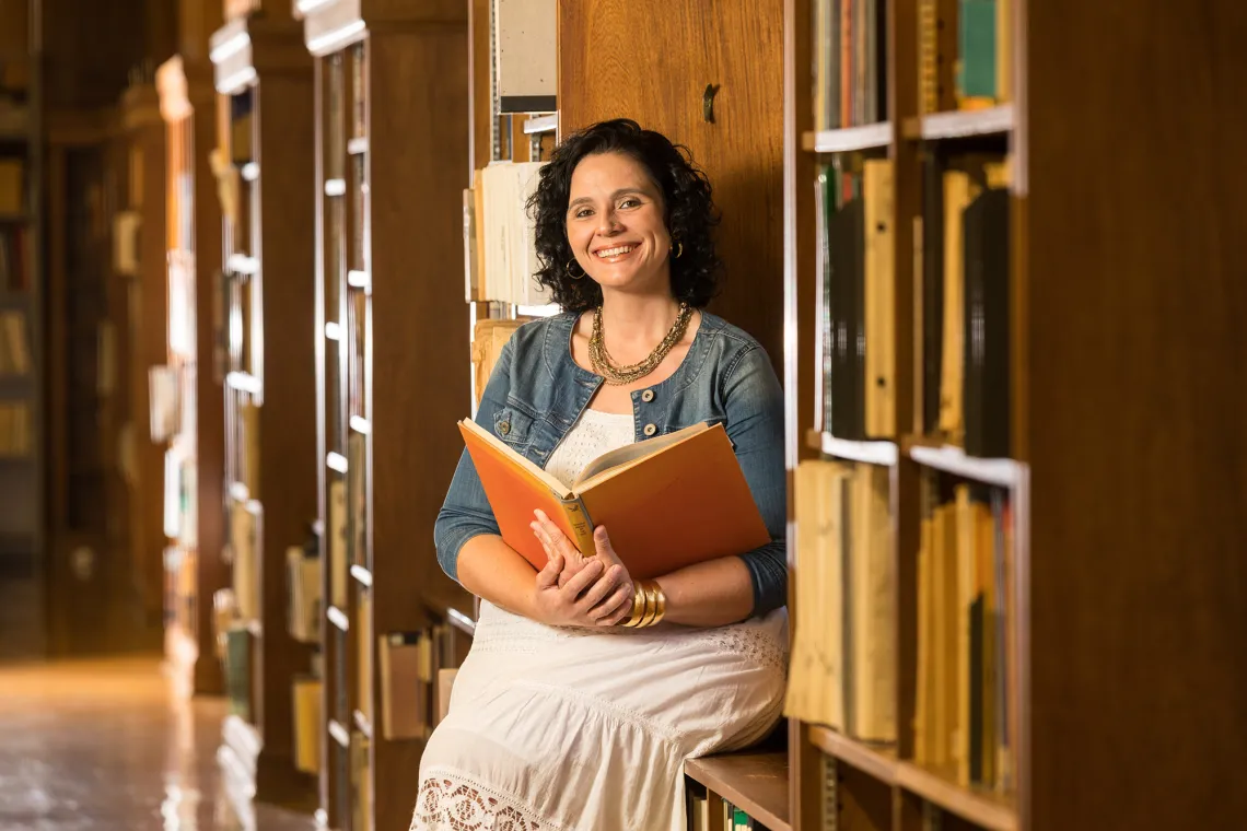 A photograph of Shyla Dogan sitting and smiling with a book in her hand