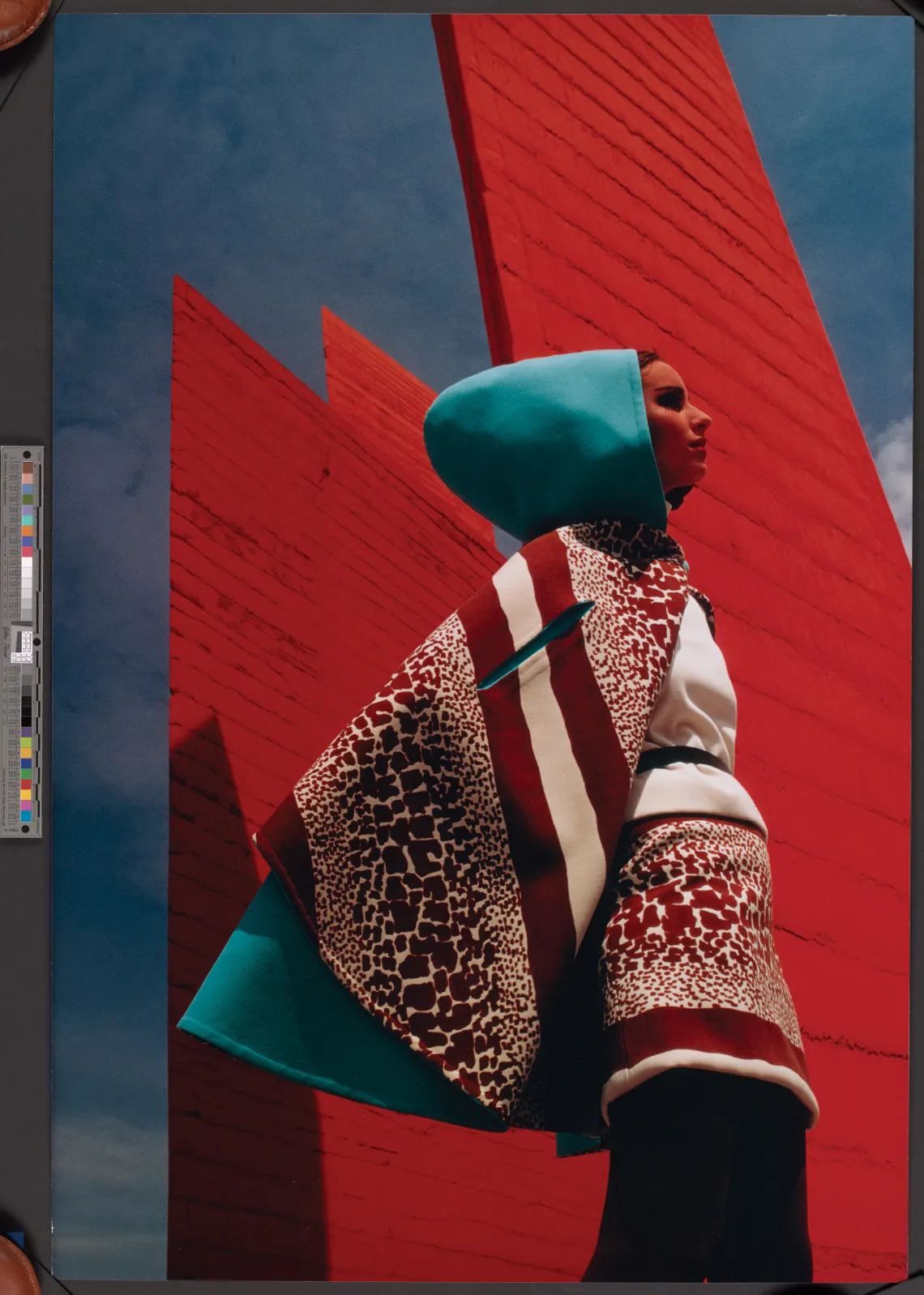 A photograph of a model wearing a bright blue cape, an elaborate animal print dress in front of three red stands