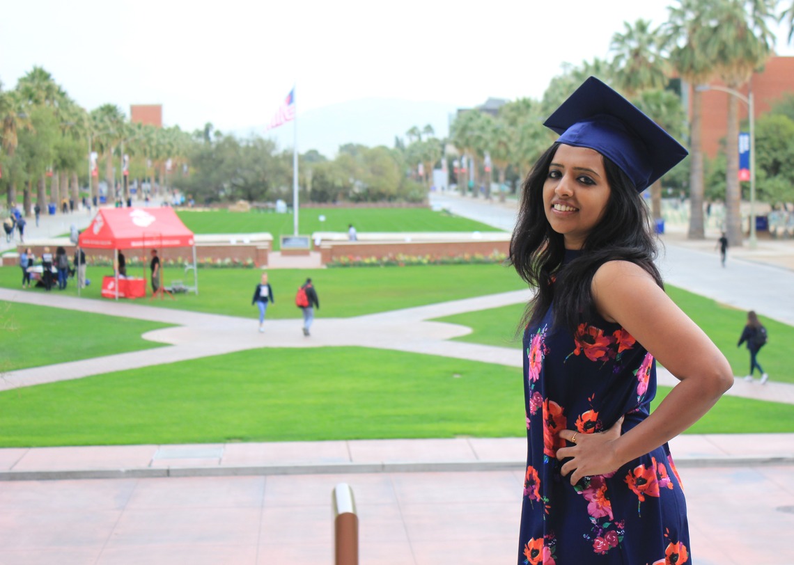 A photograph of Sonali George posing with a graduation cap in front of the UA Mall