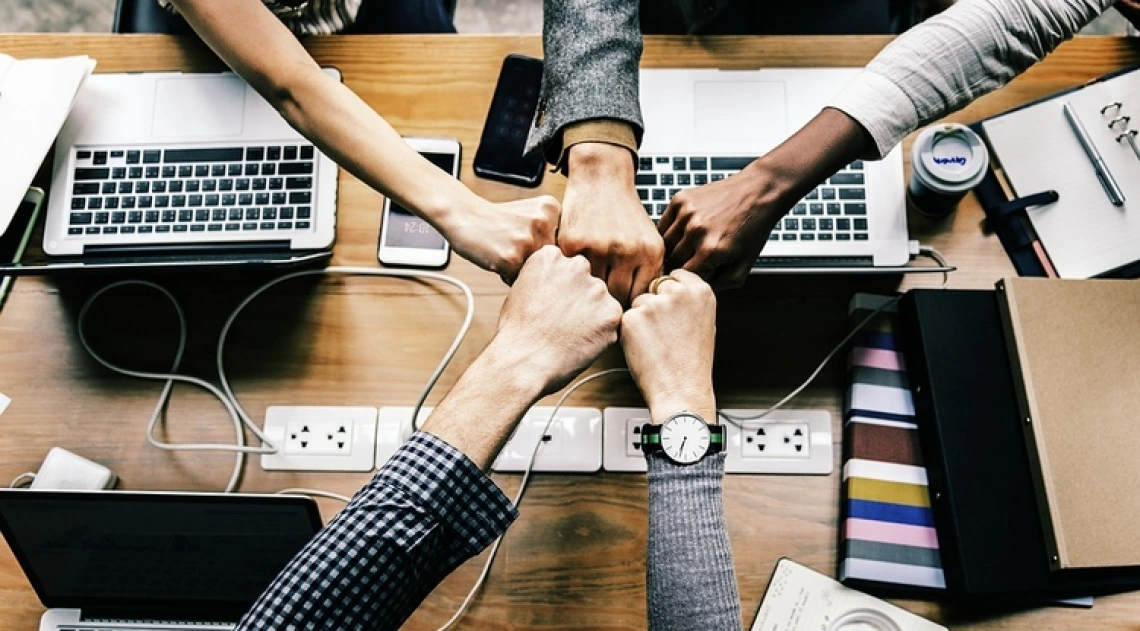 A photograph of five hands fist bumping each other over their computers and cellphones