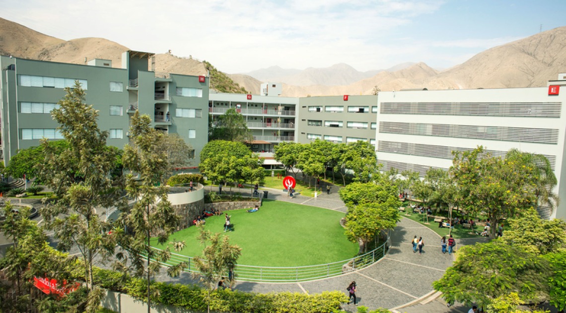 A photograph of the UA Lima building, which is surrounded by a plethora of green grass, trees and mountains