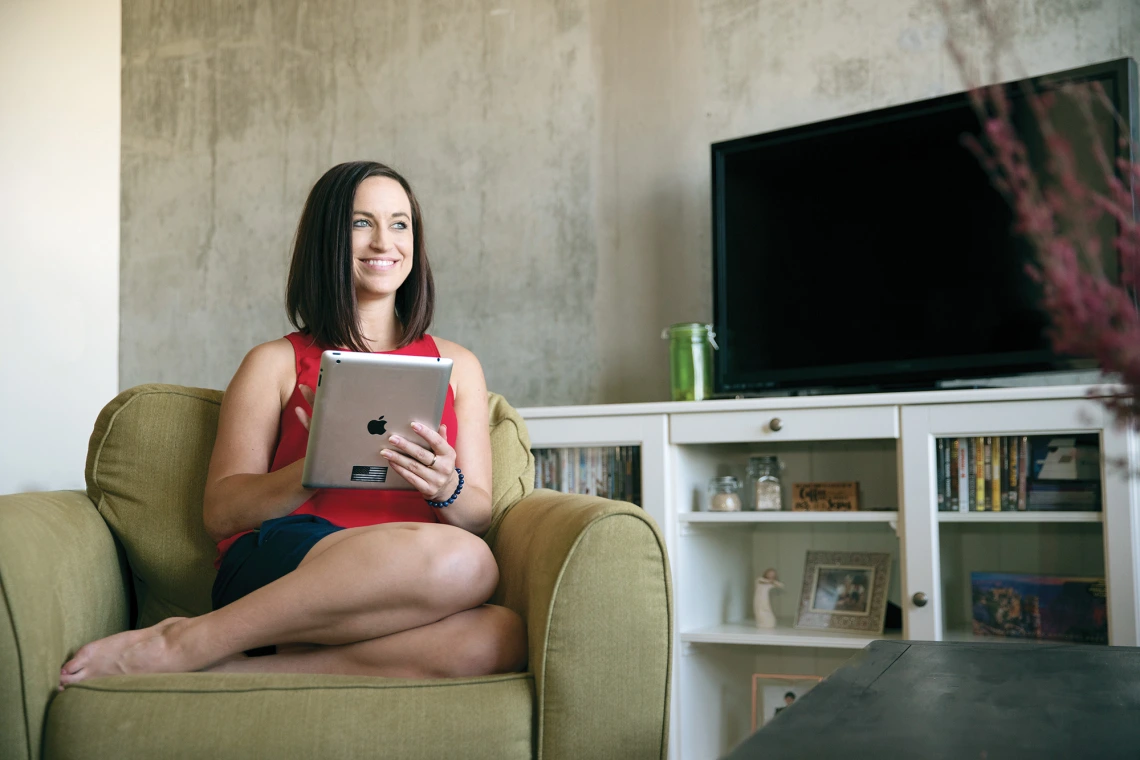 A photograph of Melissa Watkins sitting on a chair with an iPad smiling