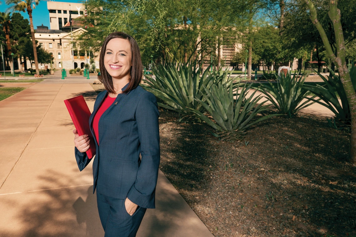 A photograph of Melissa Watkins smiling with a binder at the state's capital