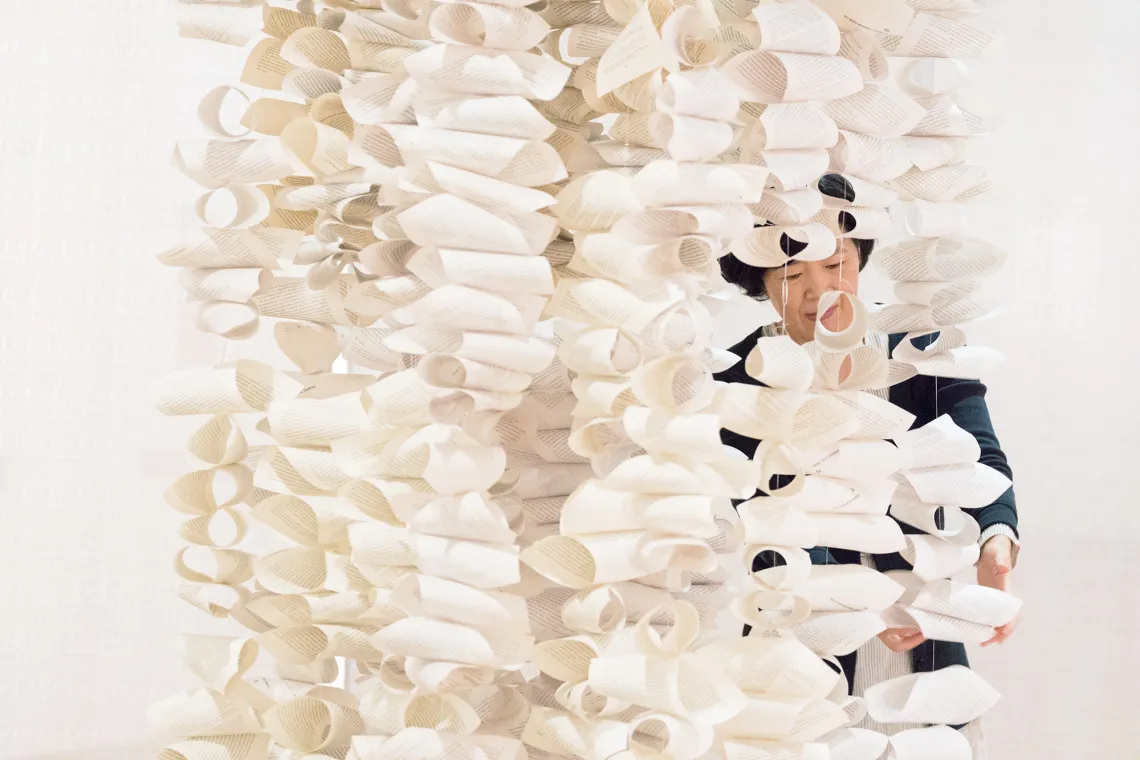 A photograph of Xinyu Zhang standing behind a paper sculpture