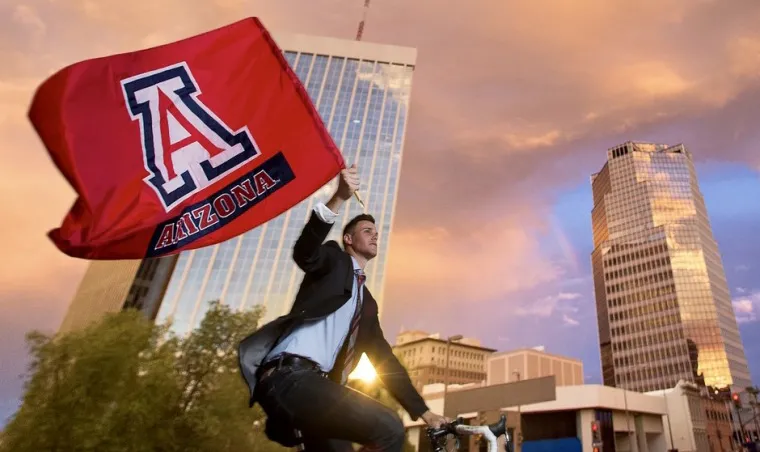 Man riding bike in downtown Tucson carrying UA flag