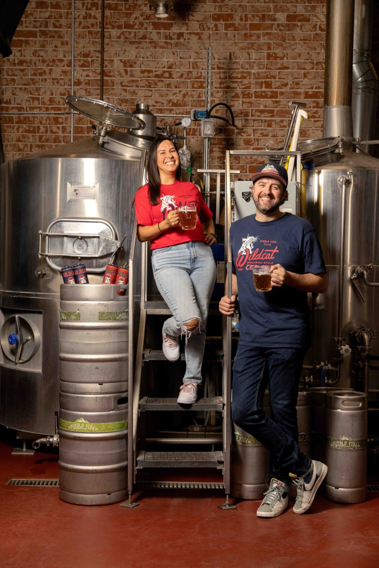 A woman and man pose near brewery equipment