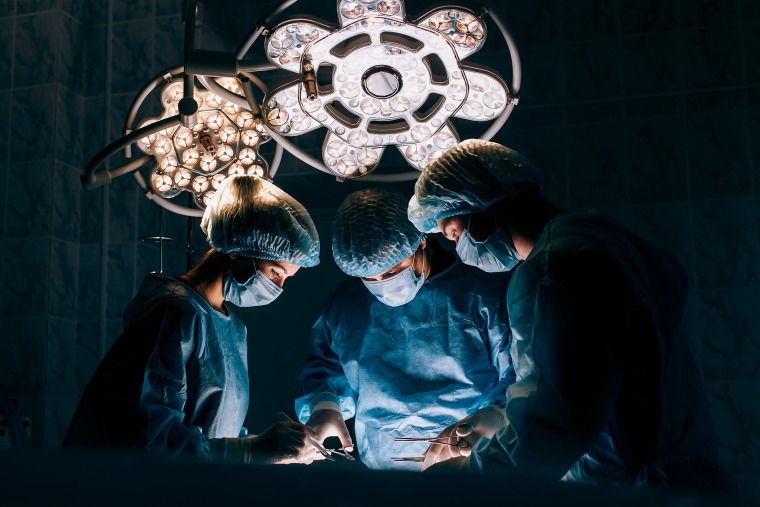Surgeons in a medical setting wearing scrubs with dramatic lighting