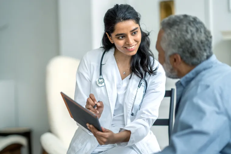 A photograph of a doctor wearing a white lab coat holding a tablet, showing it to an older adult patient. 